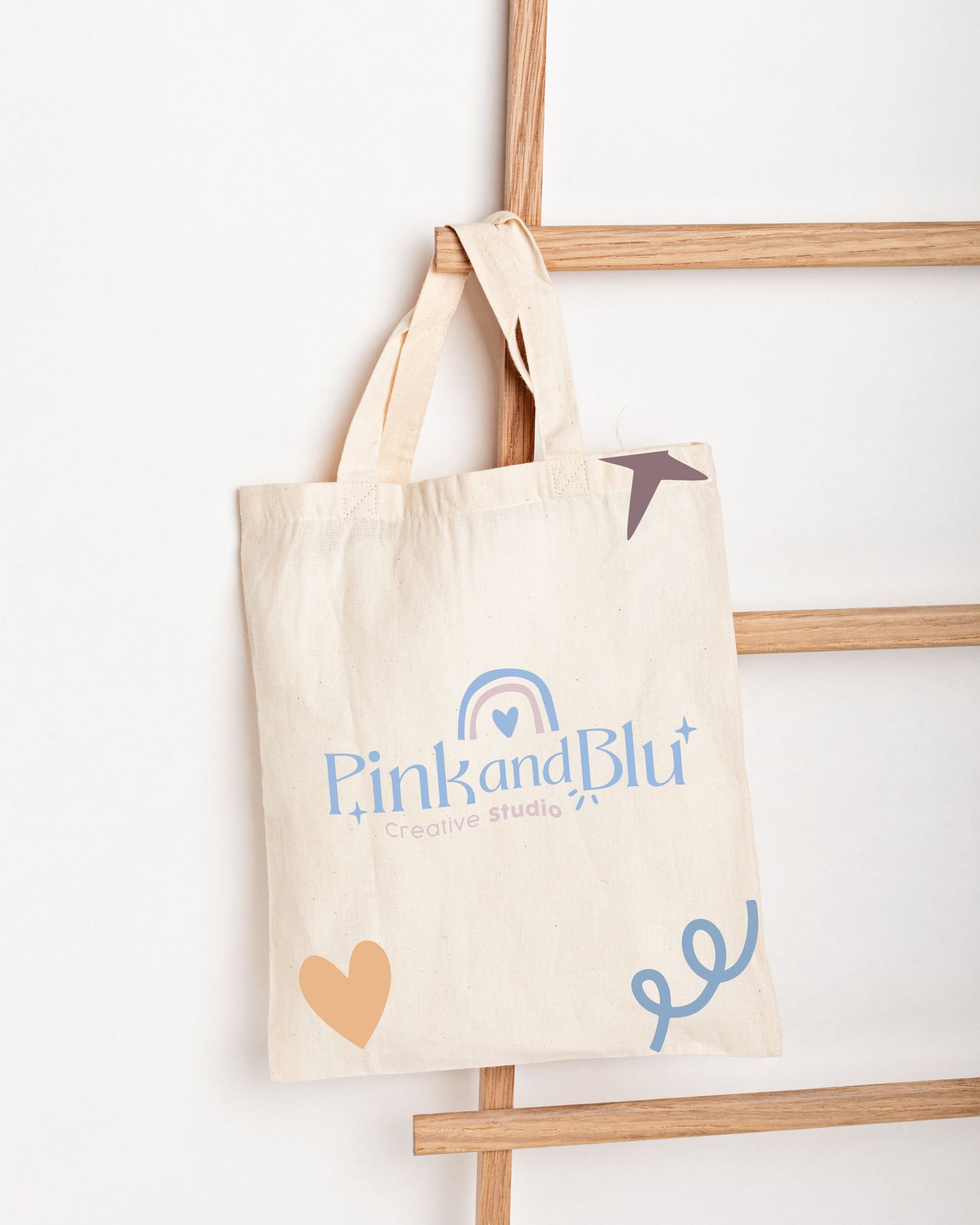 Beige tote bag with 'Pink and Blu' branding on a wooden ladder against a white background