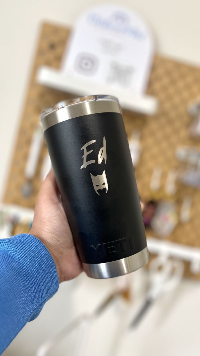 Black tumbler with 'Ed' and a cat illustration held by a person in a blue sleeve.