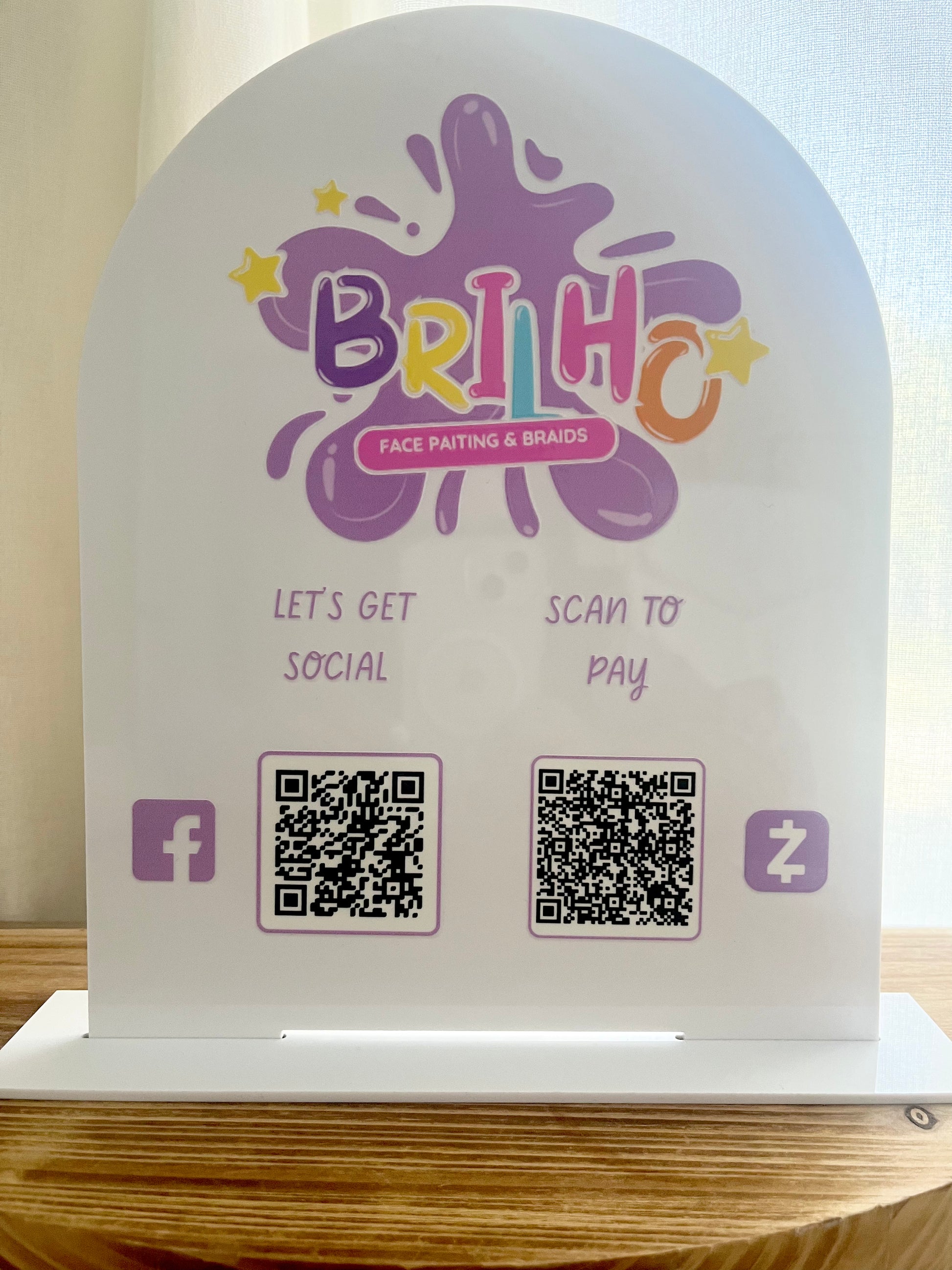 Brillo face painting and branding station with QR codes for social media and payment on a wooden surface.