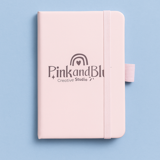 Pink notebook with 'Pink and Blk Creative Studio' logo on a light blue background