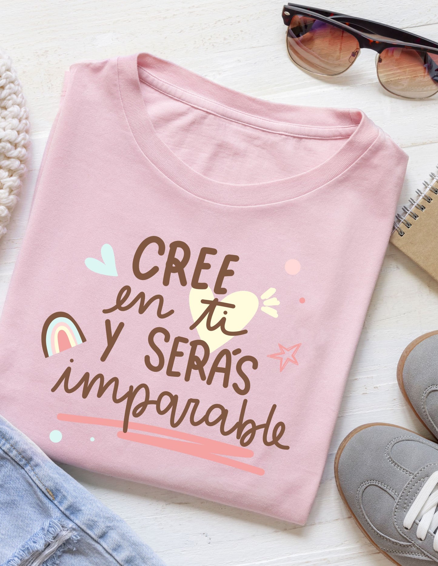 Folded pink t-shirt with motivational text on a white surface with accessories.