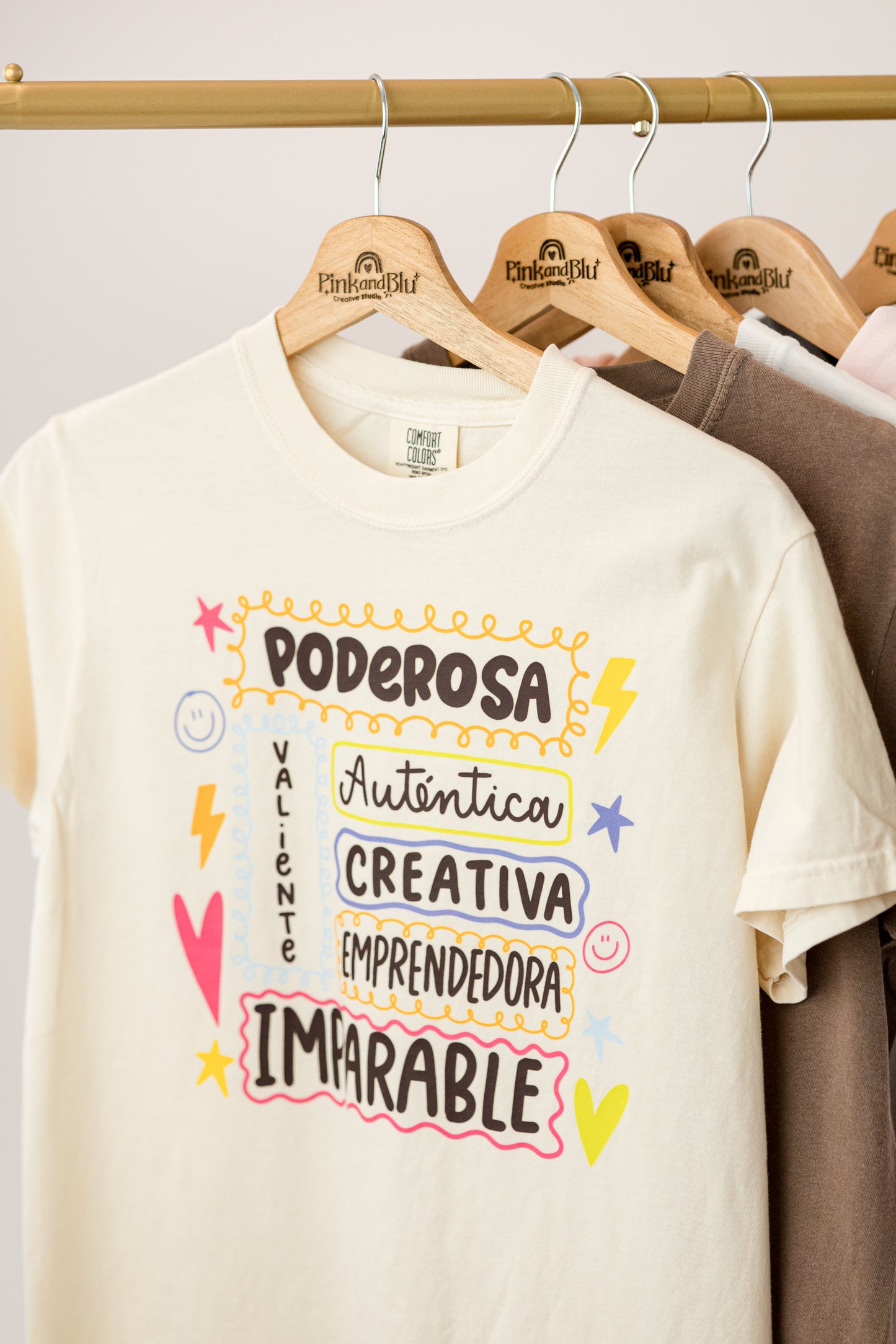 Beige t-shirt with colorful text on a wooden hanger against a neutral background