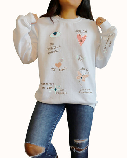 Person wearing a beige sweatshirt with text and graphics, standing against a plain background