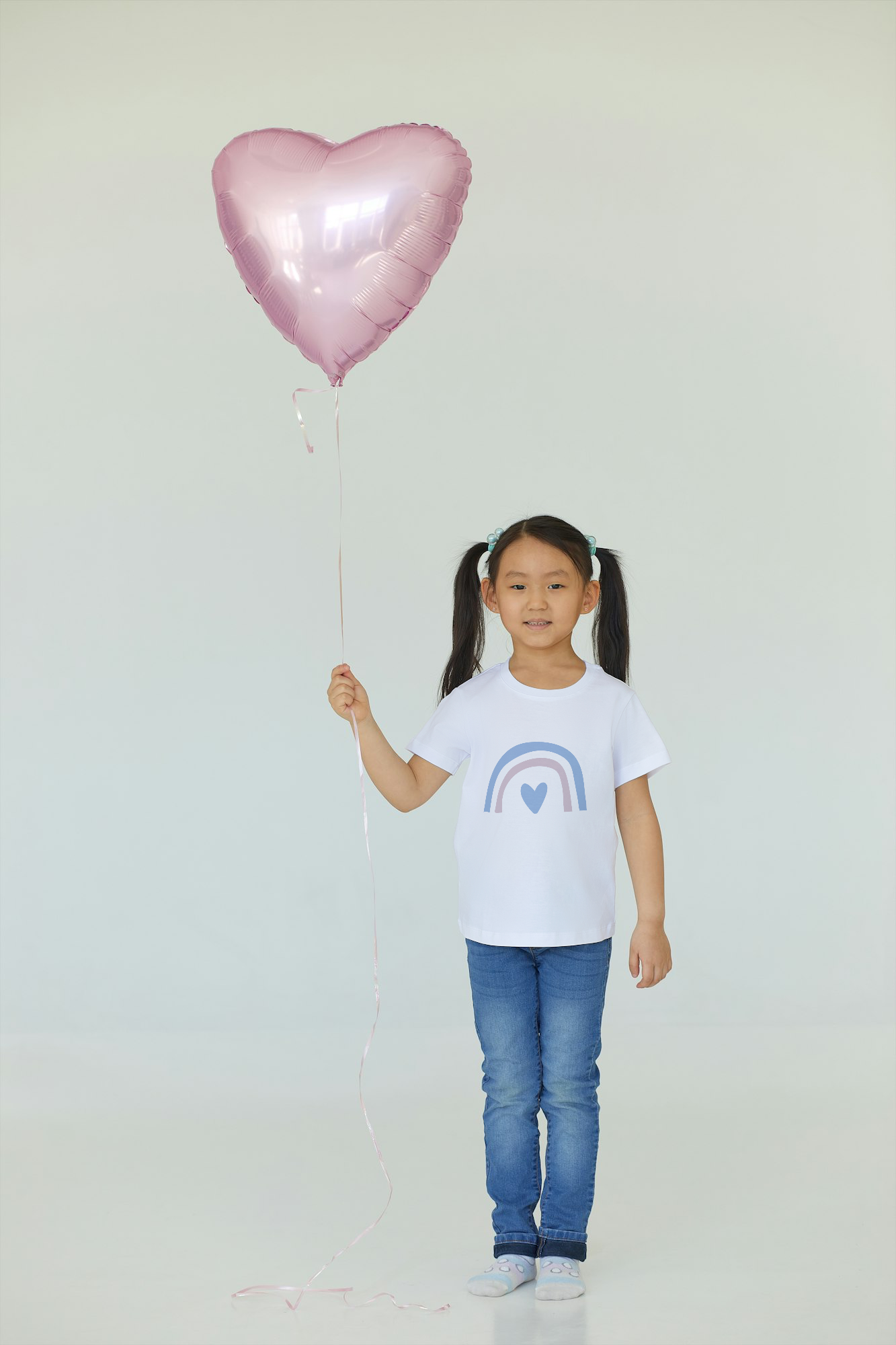 Child holding a pink heart-shaped balloon against a plain background