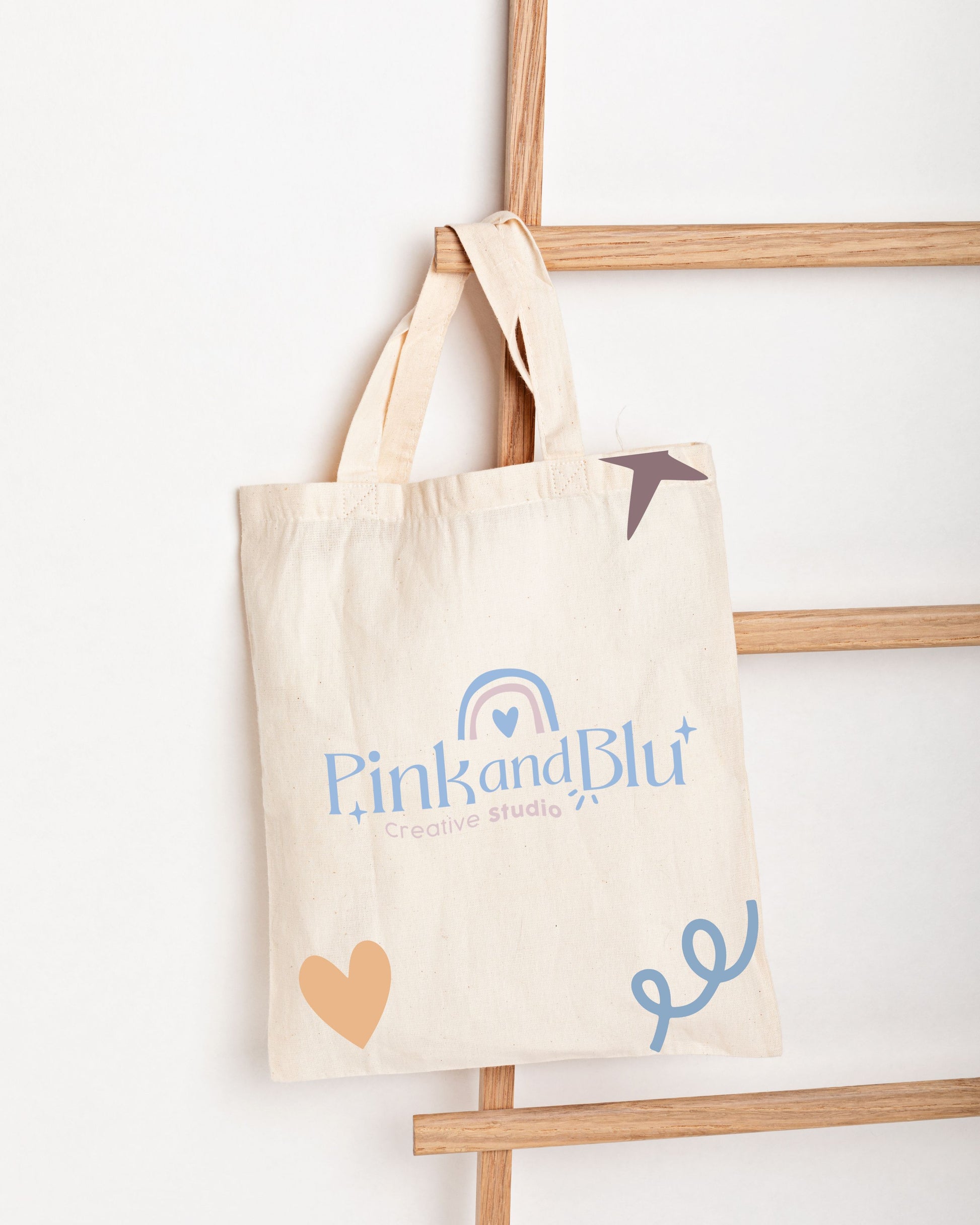 Beige tote bag with 'Pink and Blu' branding on a wooden ladder against a white background