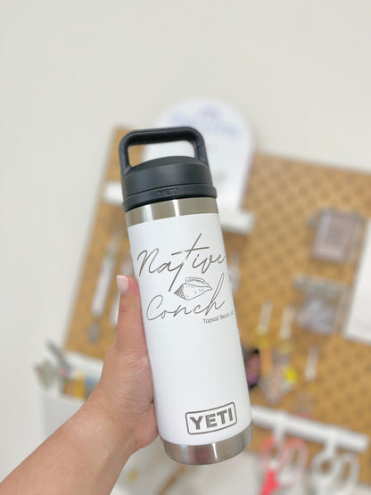 White YETI water bottle with black lid held by a hand against a blurred background